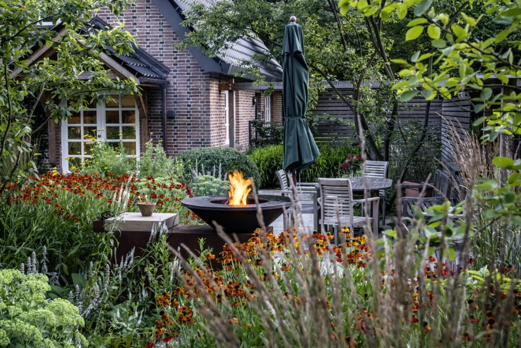 Terrasse Beete Stauden Außenküche Feuer Abendstimmung Tisch Stühle Gärten des Jahres